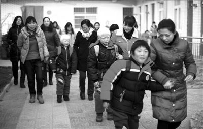 　　在福利院老师的带领下，孩子们背起书包出发去学校。本报记者王苡萱摄出发去学校前，一名小姑娘蹲在地上认真收拾书包。本报记者王苡萱摄